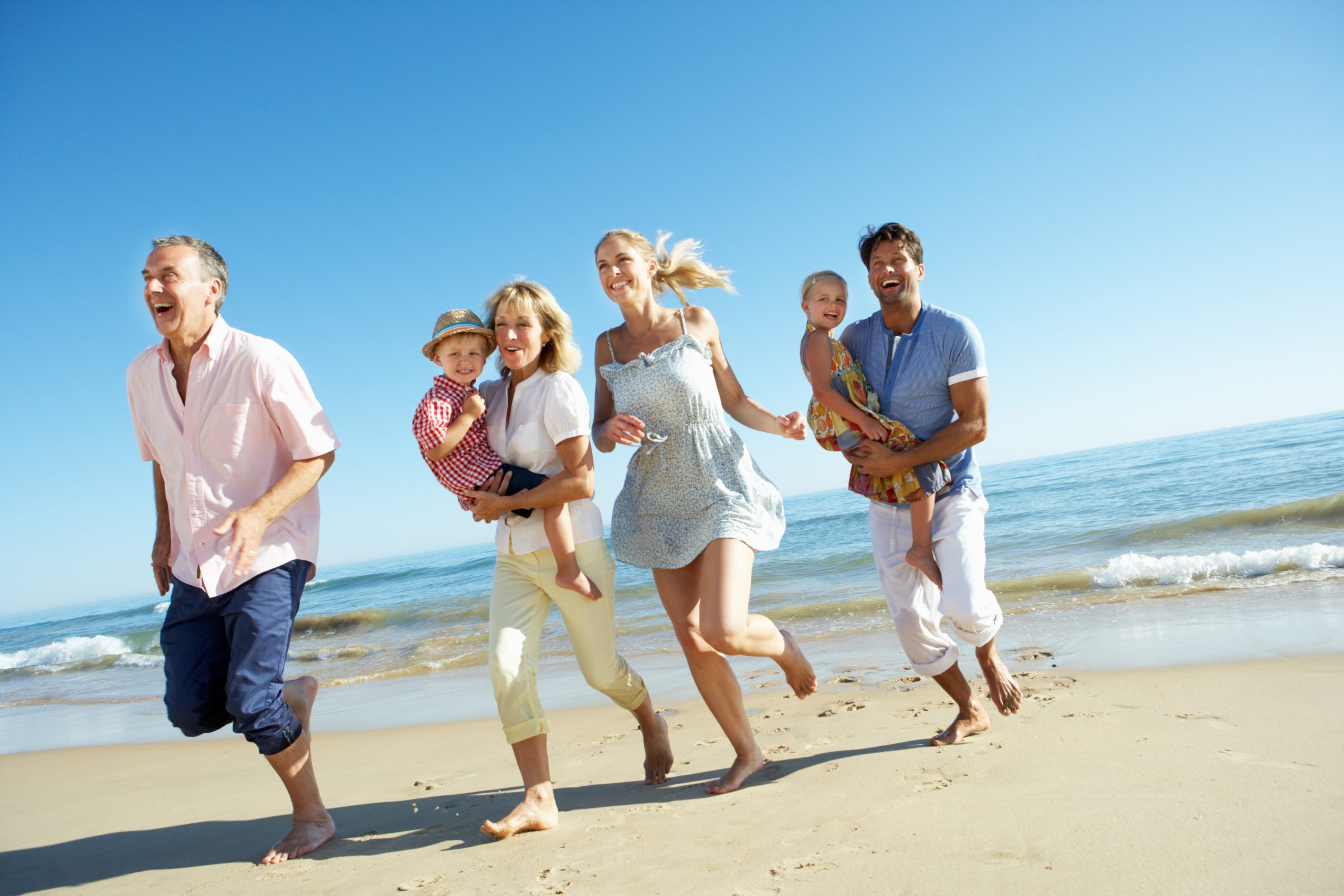 Multi Generation Family Enjoying Holiday Running Along Beach